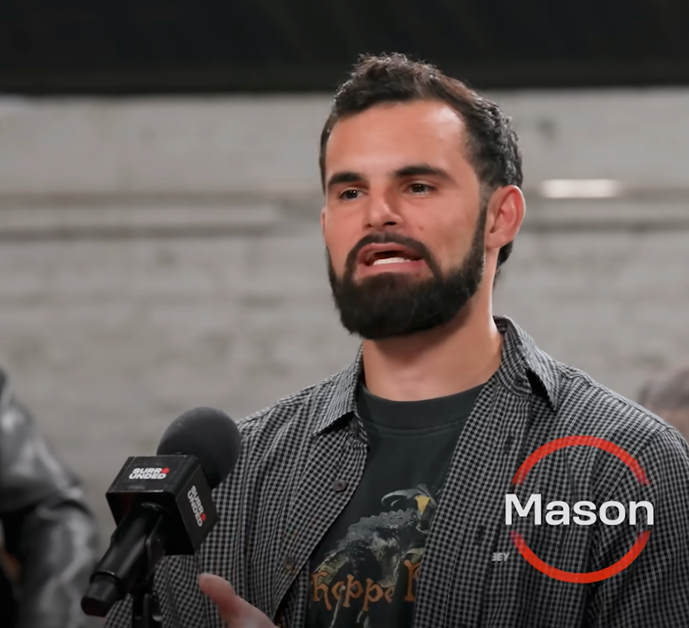 Mann ved navn Mason snakker på en paneldiskusjon med mikrofoner foran. Bakgrunn viser andre paneldeltakere
