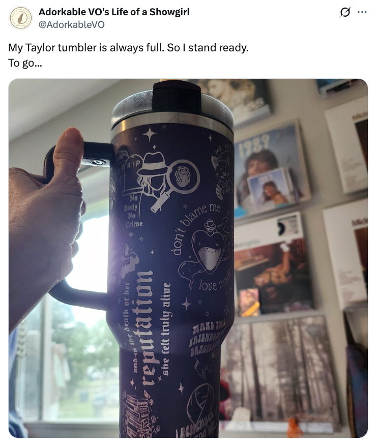 Person holds a tumbler decorated with text and graphics, surrounded by photos. Text on the tumbler relates to a musical theme