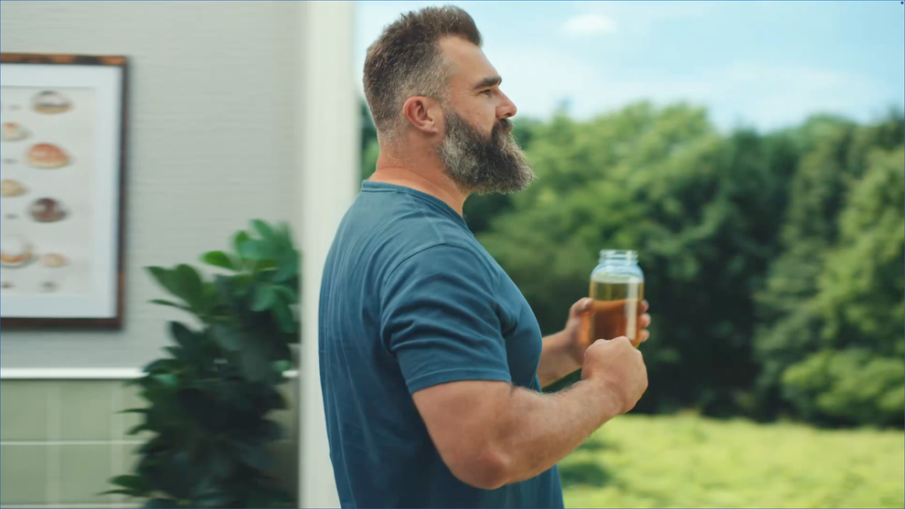 Man with a beard holding a jar of tea stands outdoors, looking into the distance