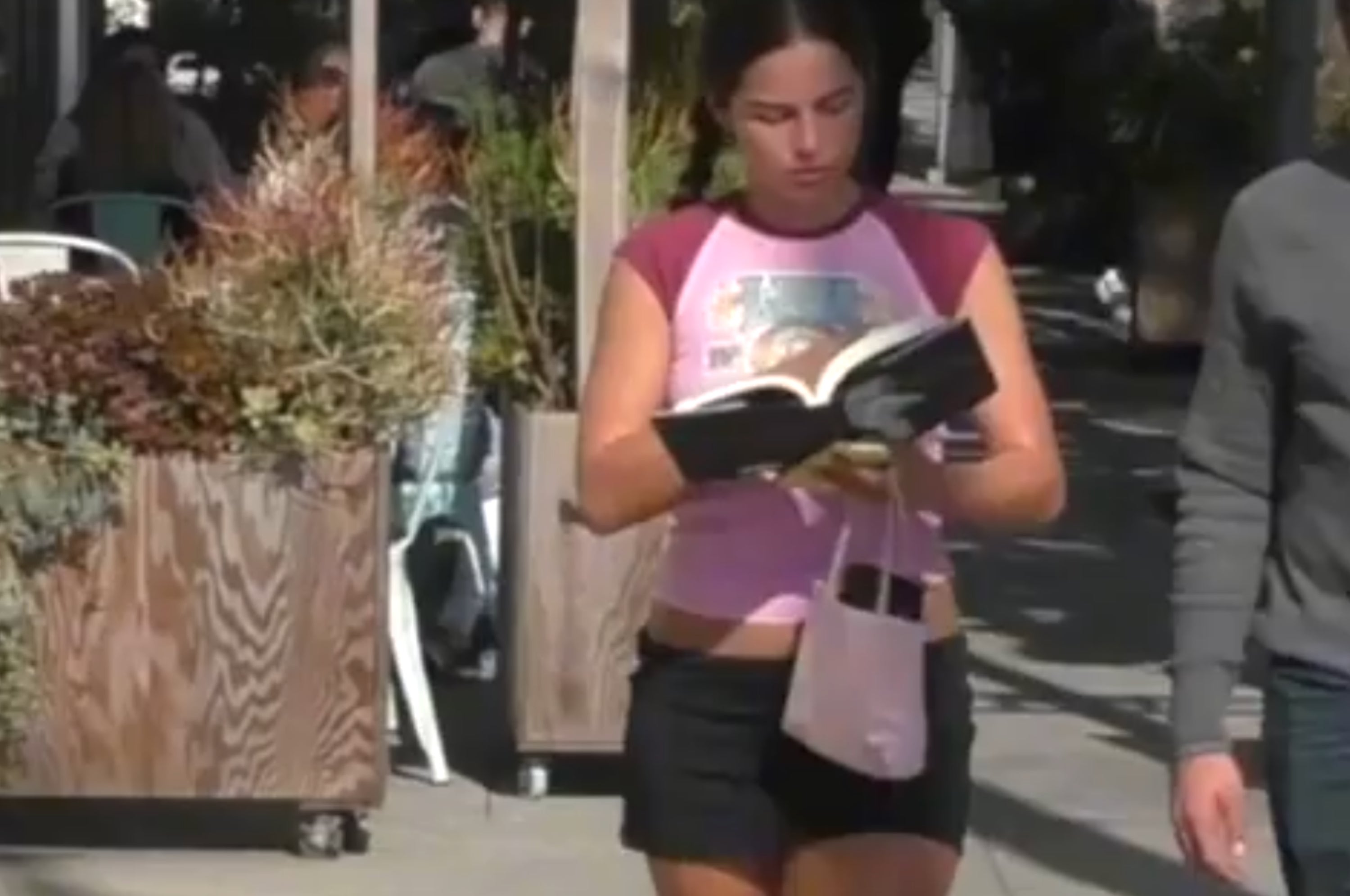 Woman in casual wear reads Britney Spears' memoir while outside on a sunny day, appearing engaged