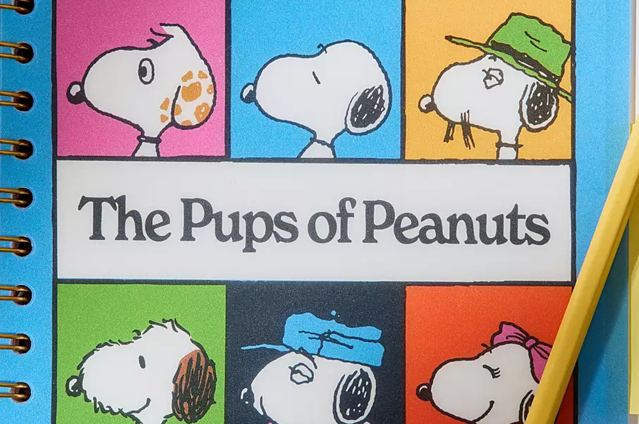Notebook with "The Pups of Peanuts" cover featuring Snoopy illustrations and a pencil placed on it