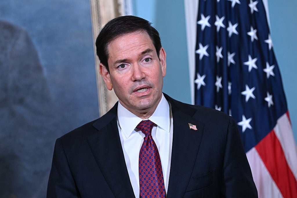 Marco Rubio, i dress og slips, snakker foran et amerikansk flagg