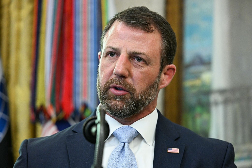 Markwayne Mullin, i dress med en amerikansk flaggnål, snakker ved et podium med flagg i bakgrunnen