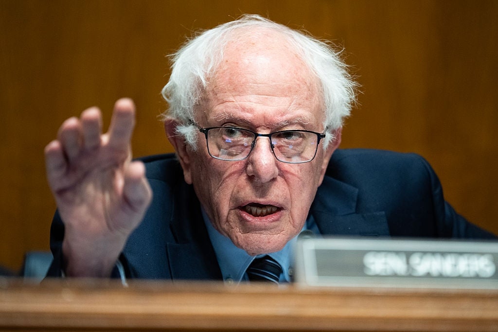 Bernie Sanders snakker lidenskapelig ved et podium i formelle omgivelser, iført dress og briller, og understreker et poeng med hånden hevet