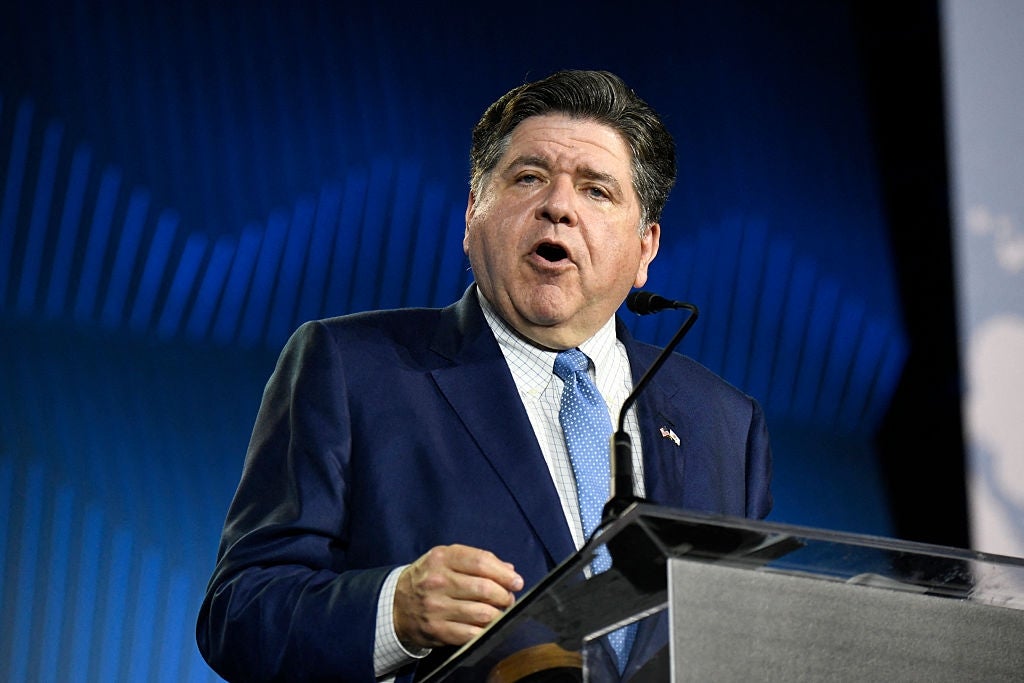 JB Pritzker i dress og slips snakker lidenskapelig ved et podium under et arrangement