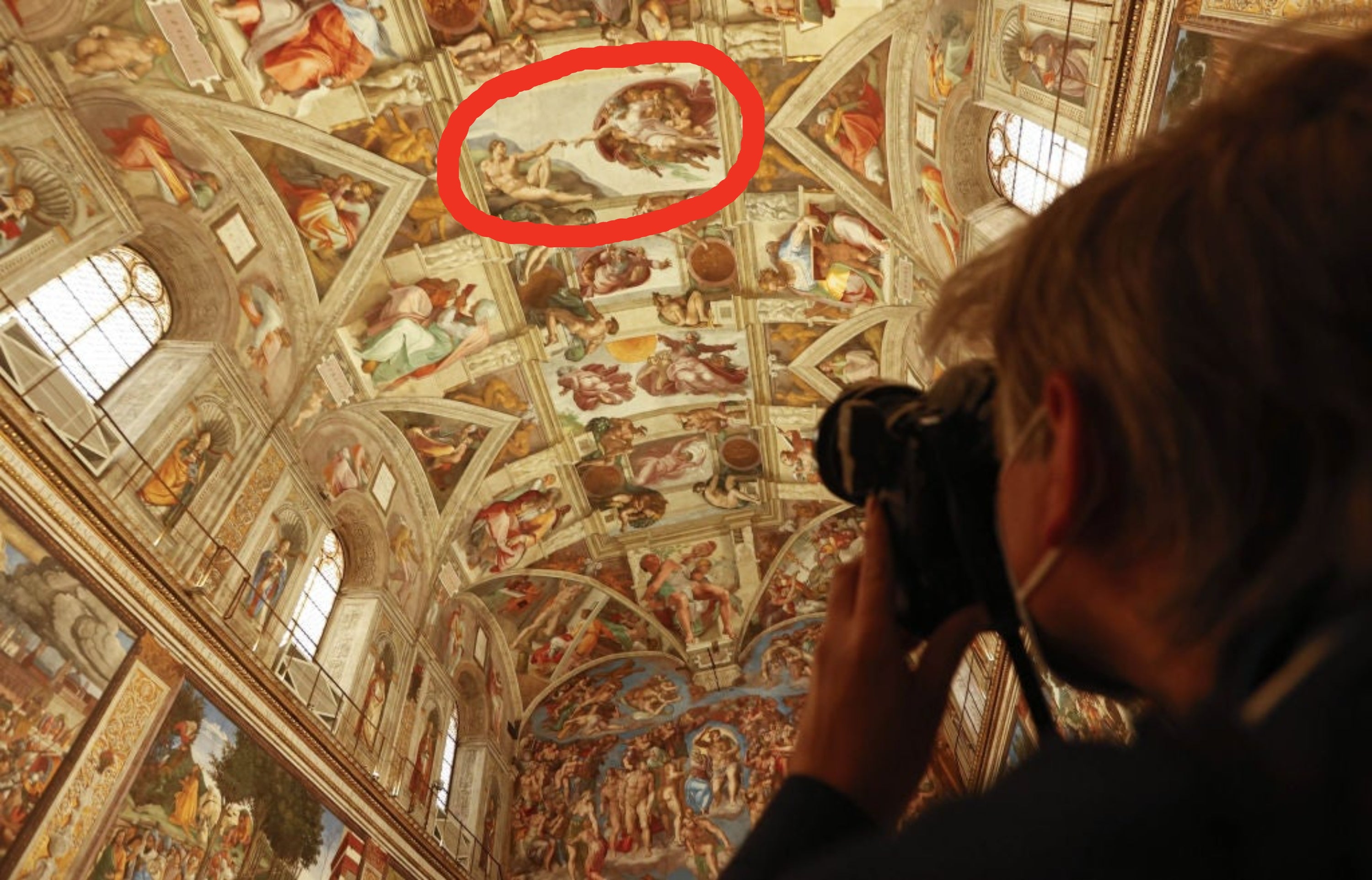 A person photographs the intricate frescoes on the ceiling of the Sistine Chapel, showcasing its renowned Renaissance art