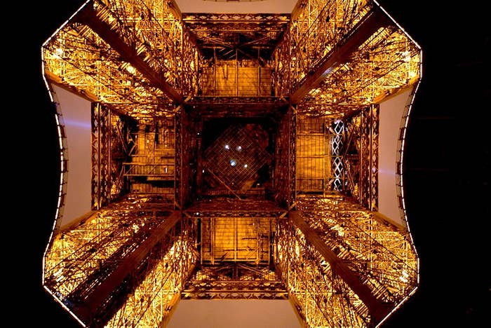 View looking up from beneath the Eiffel Tower, showcasing its intricate iron framework against the sky when it's lit up