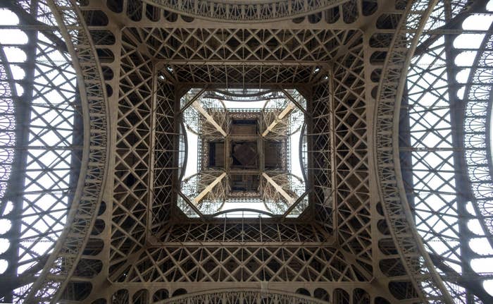 View from underneath a lattice metal structure, looking up into a symmetrical pattern; the Eiffel Tower from below