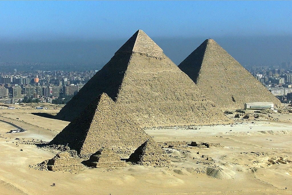 The Great Pyramids of Giza stand tall in the desert with the cityscape visible in the background