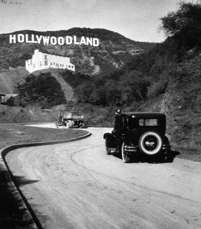 Vintage photo of cars approaching the "Hollywoodland" sign on a dirt road in hilly terrain