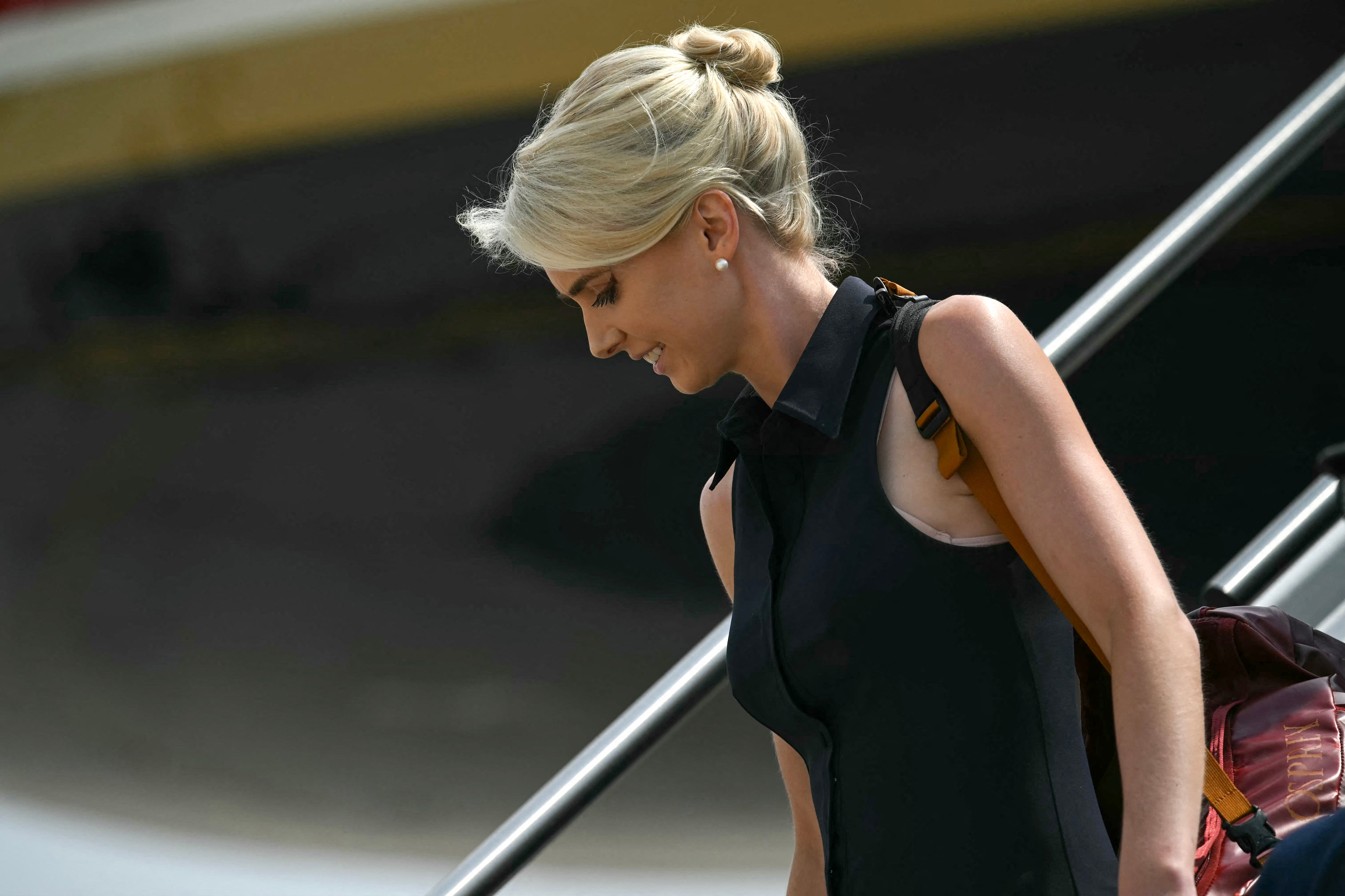 Person with blonde hair in a bun, wearing a sleeveless dress, descends airplane stairs