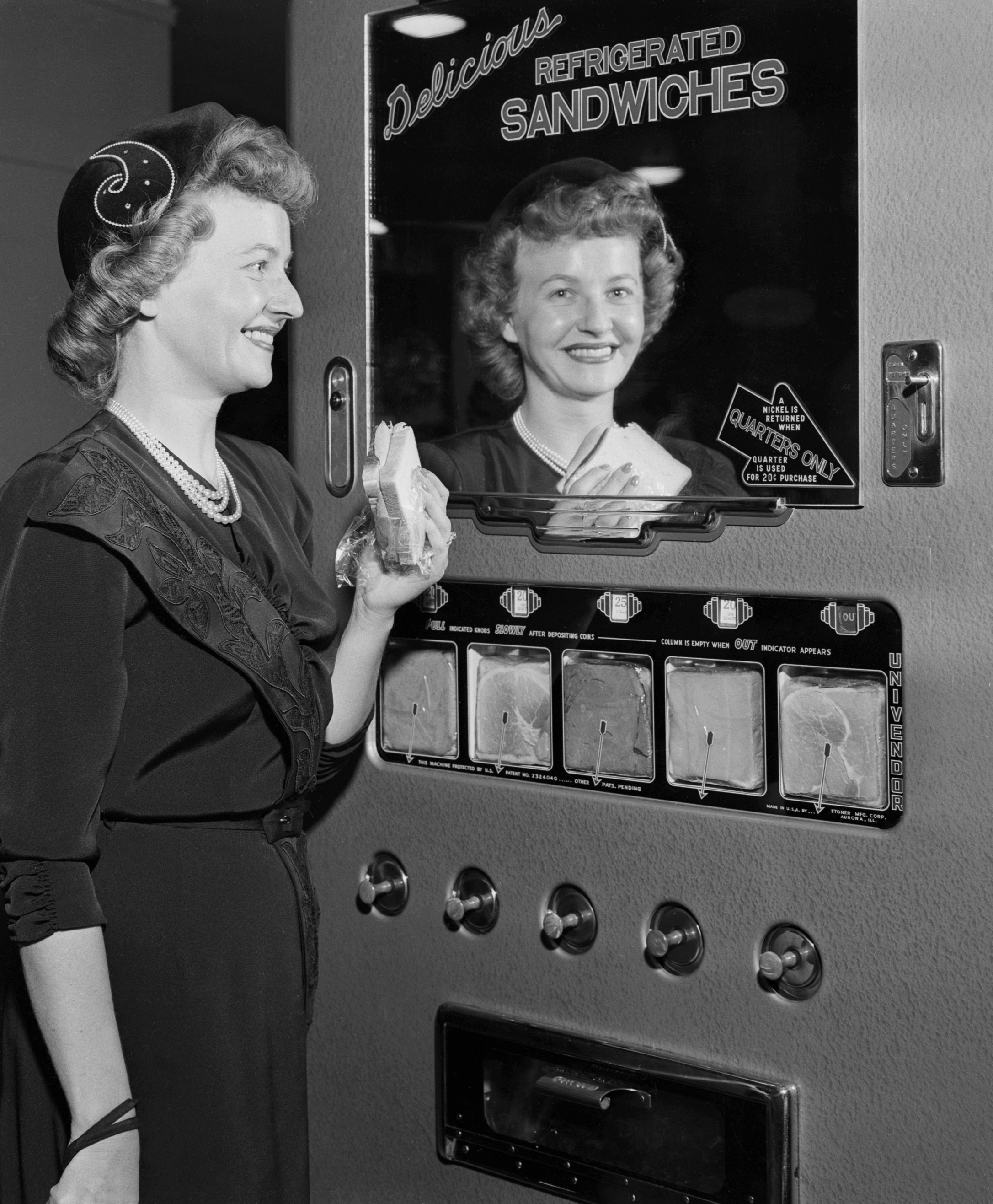 Woman using a vintage sandwich vending machine, holding a sandwich while smiling at her reflection in the machine's mirrored panel