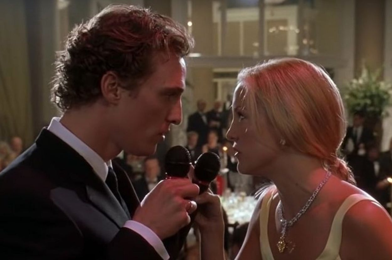 Two people in formal attire holding microphones, facing each other intently in a ballroom setting