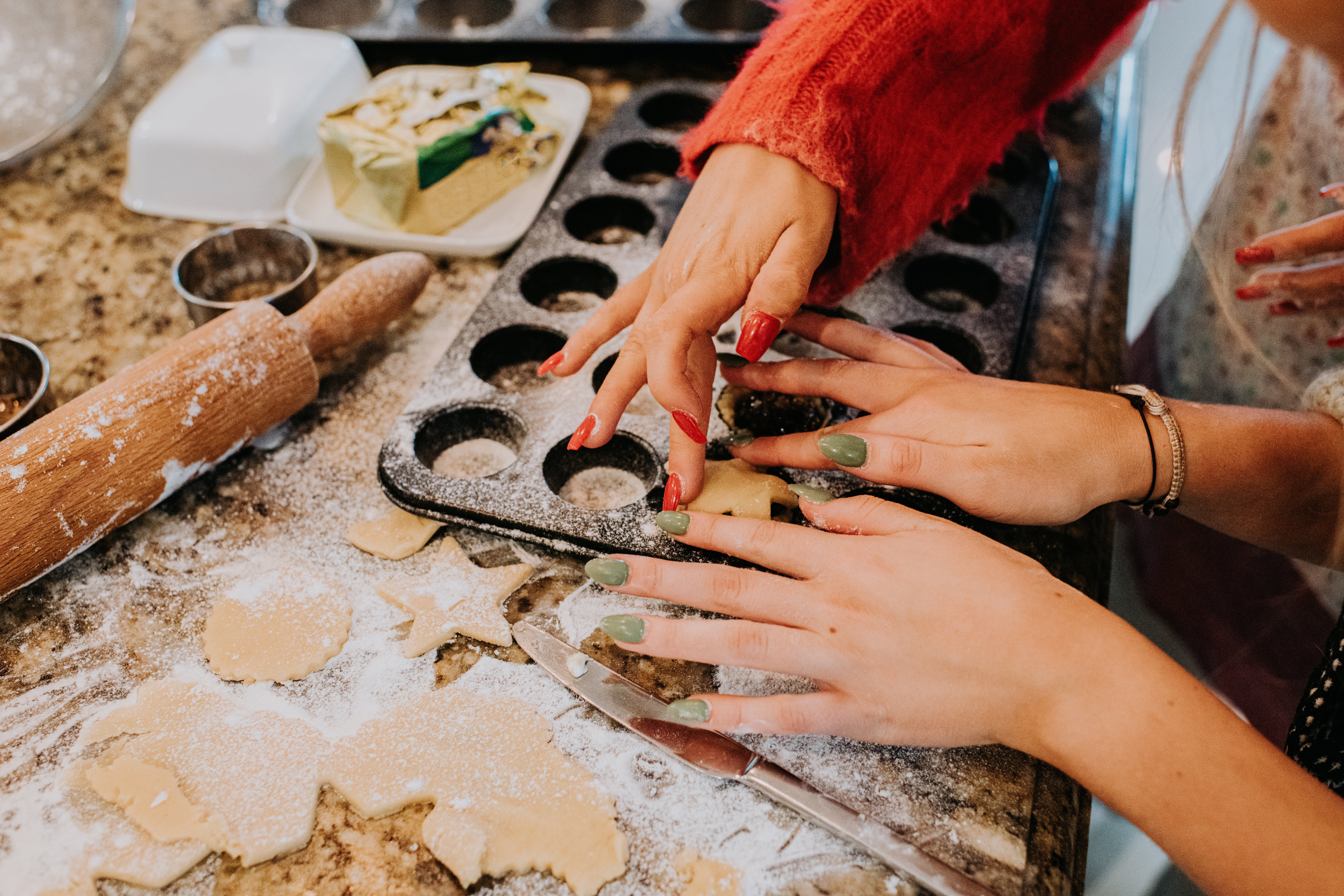 Hands cutting dough into shapes on a floured counter, surrounded by baking tools and a tray of cookies