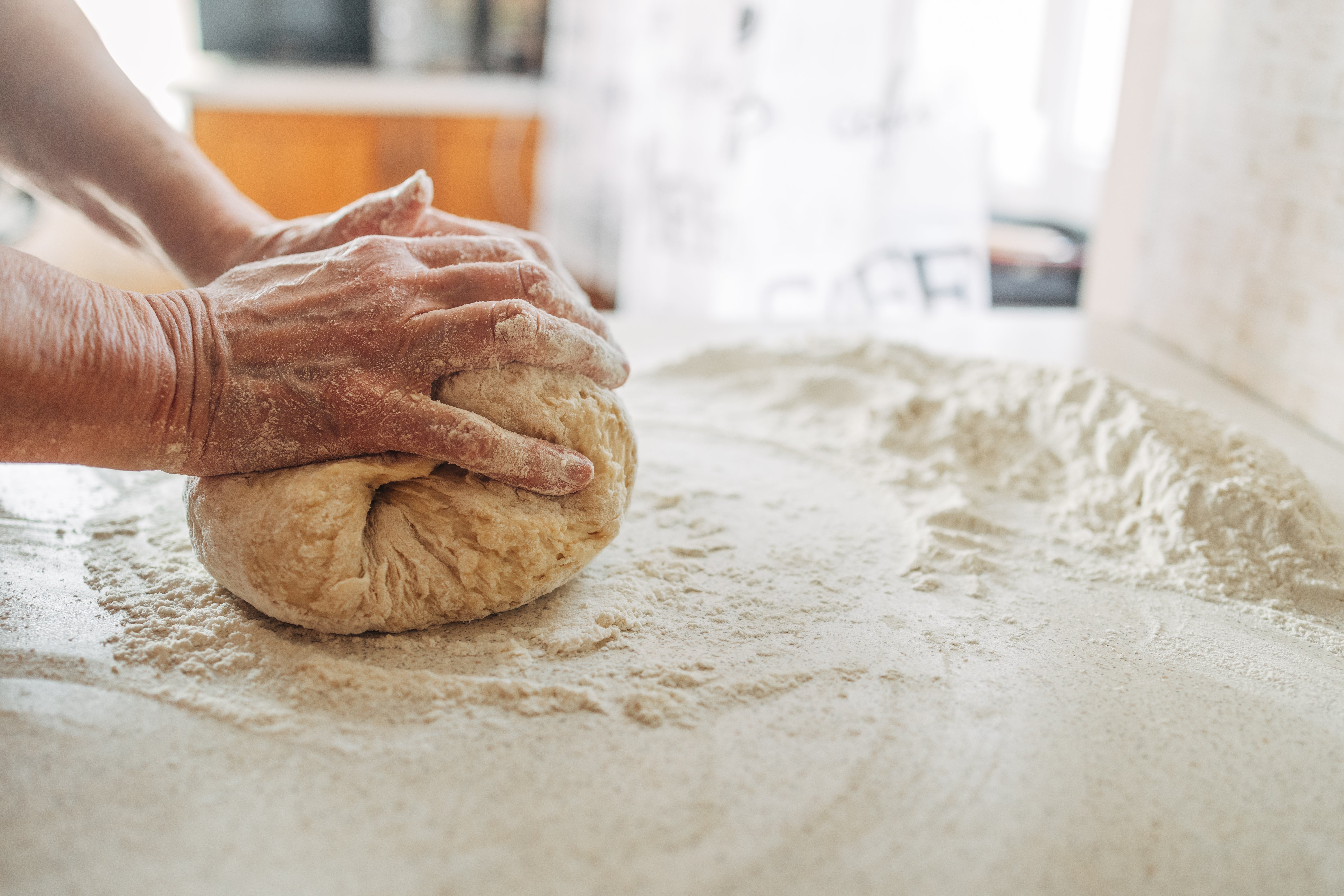 Hands kneading dough on a flour-dusted surface, preparing to bake