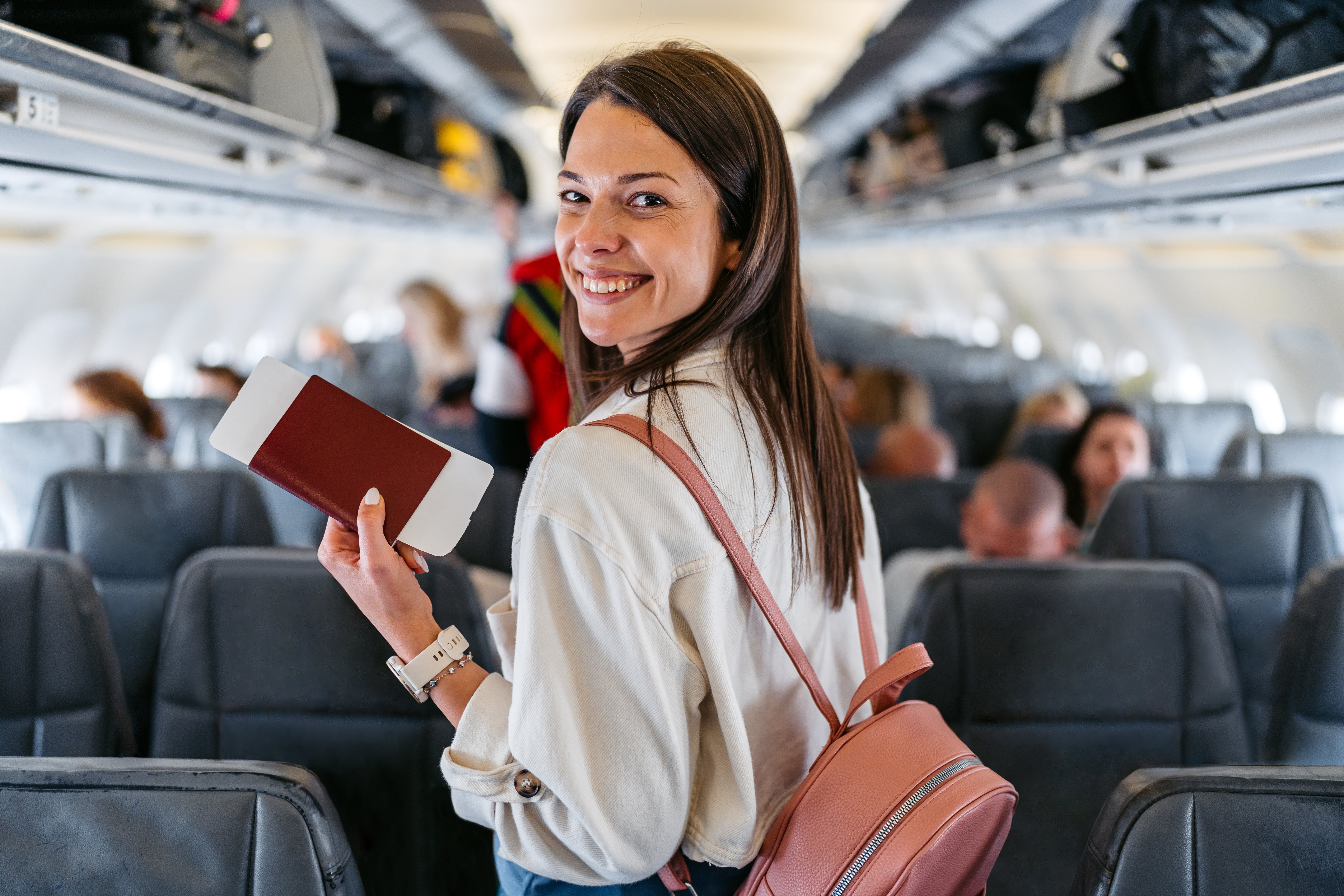Person holding a passport and boarding pass, smiling while walking down an airplane aisle