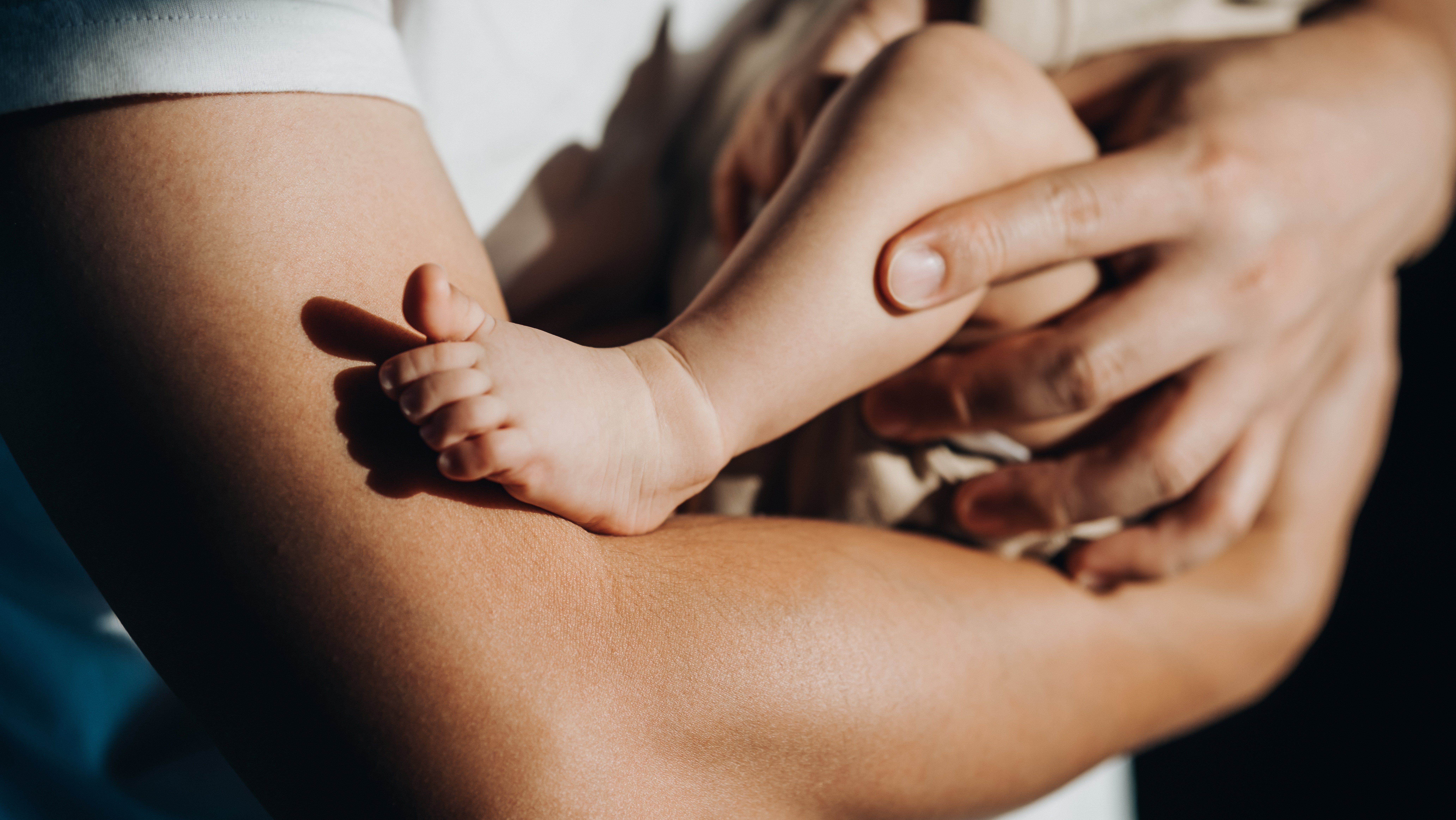 Adult holding a newborn, gently cradling the baby's head and feet in their arms