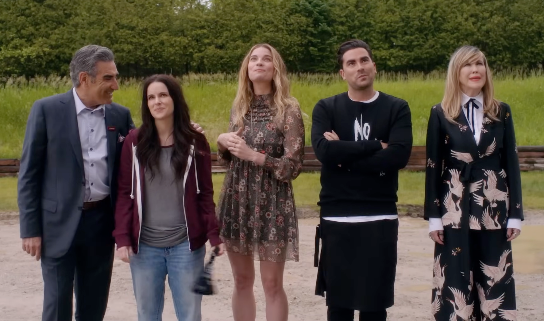 Five people stand outdoors, dressed in various casual and stylish outfits