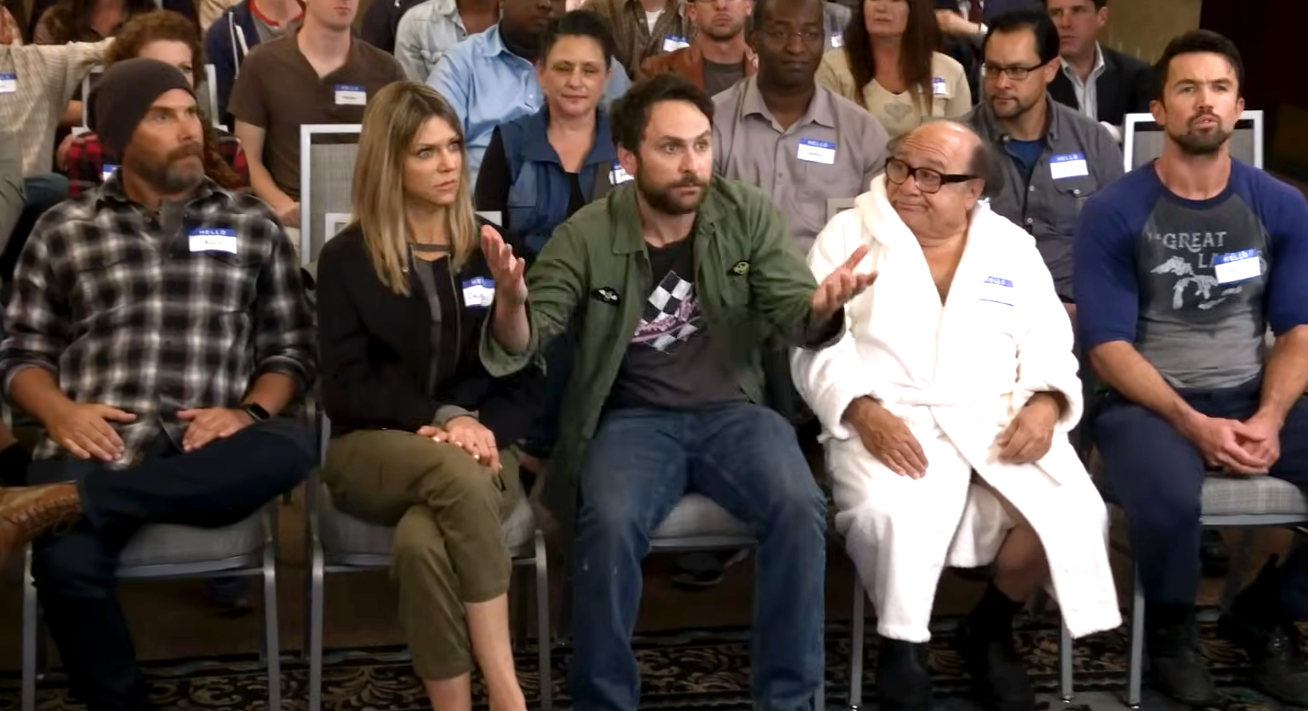 Group of people sitting in chairs during an event; one person gestures expressively while others look on attentively
