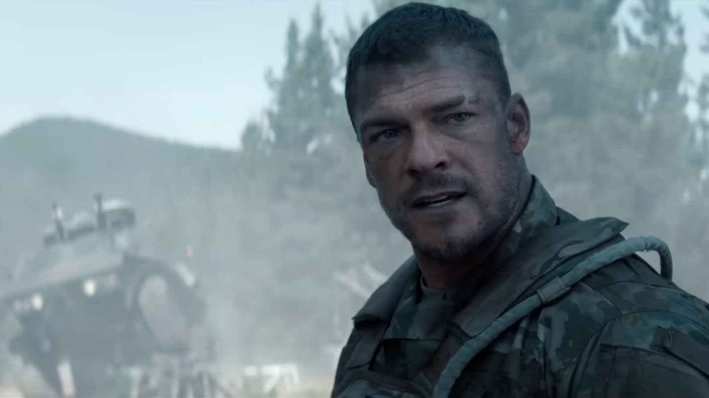 Man in military uniform looks determined in a misty, wooded area with a tipped-over vehicle in the background