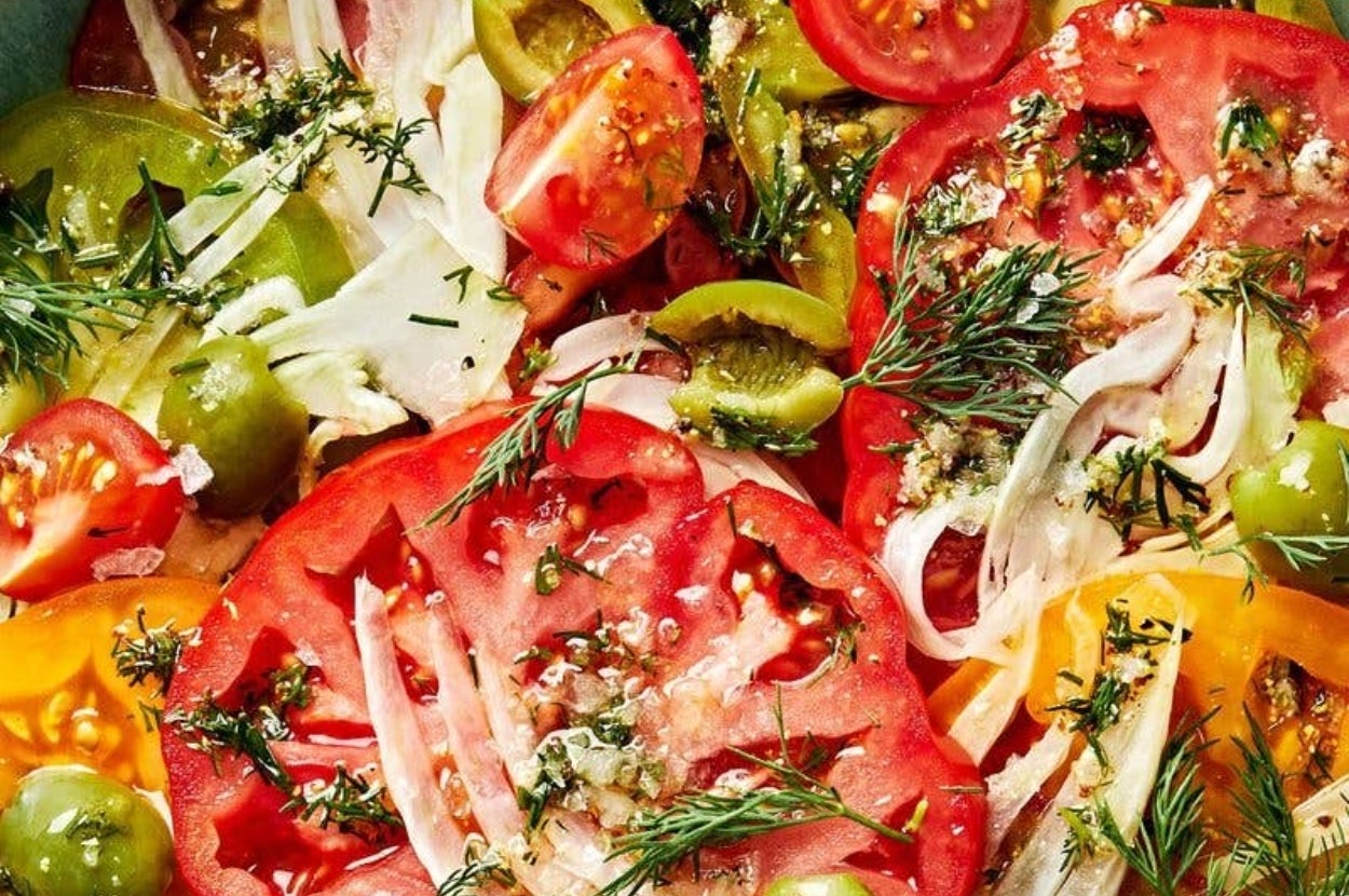 Close-up of a fresh salad with sliced tomatoes, onions, olives, and herbs