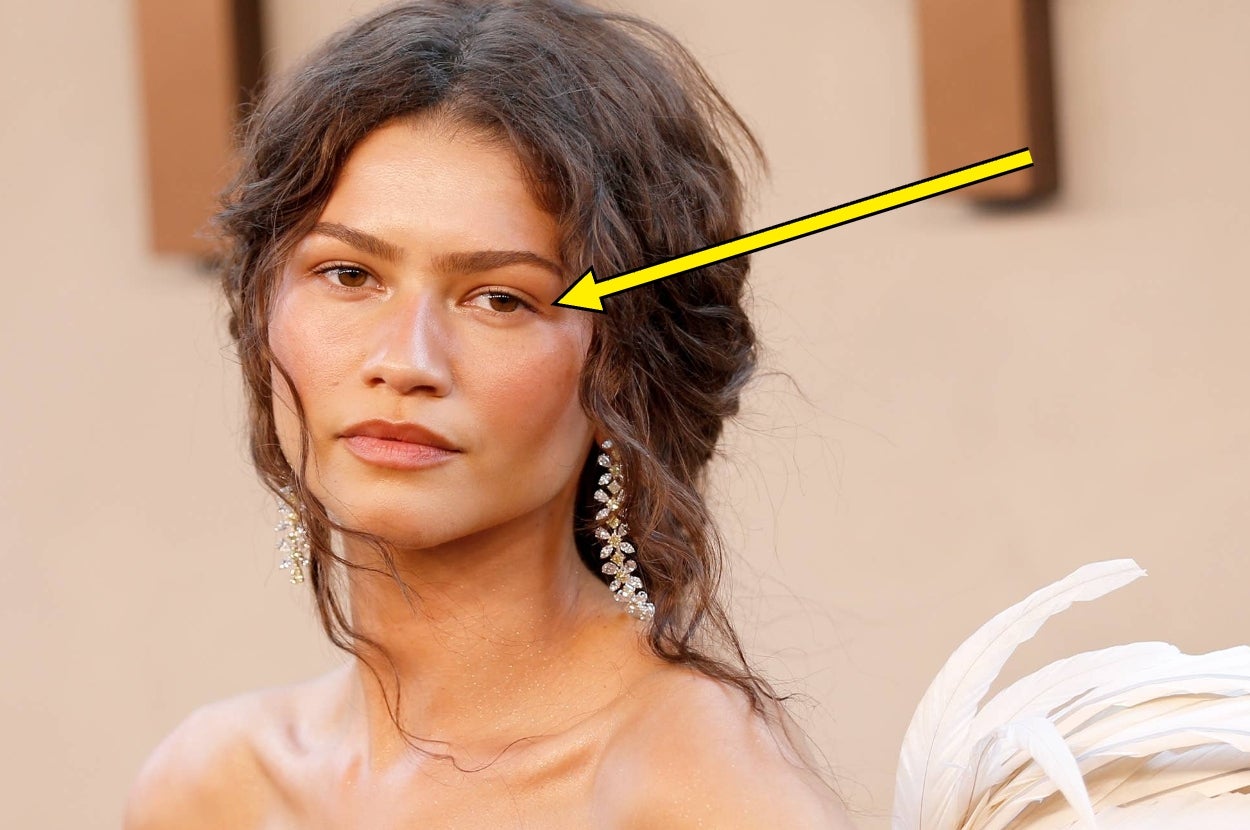 Person on red carpet with delicate earrings and a feather-detail dress, looking towards the camera