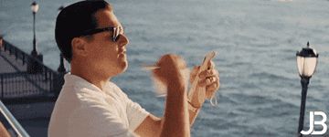 Leonardo DiCaprio as Jordan Belfort, throwing money into the air joyfully by a scenic waterfront