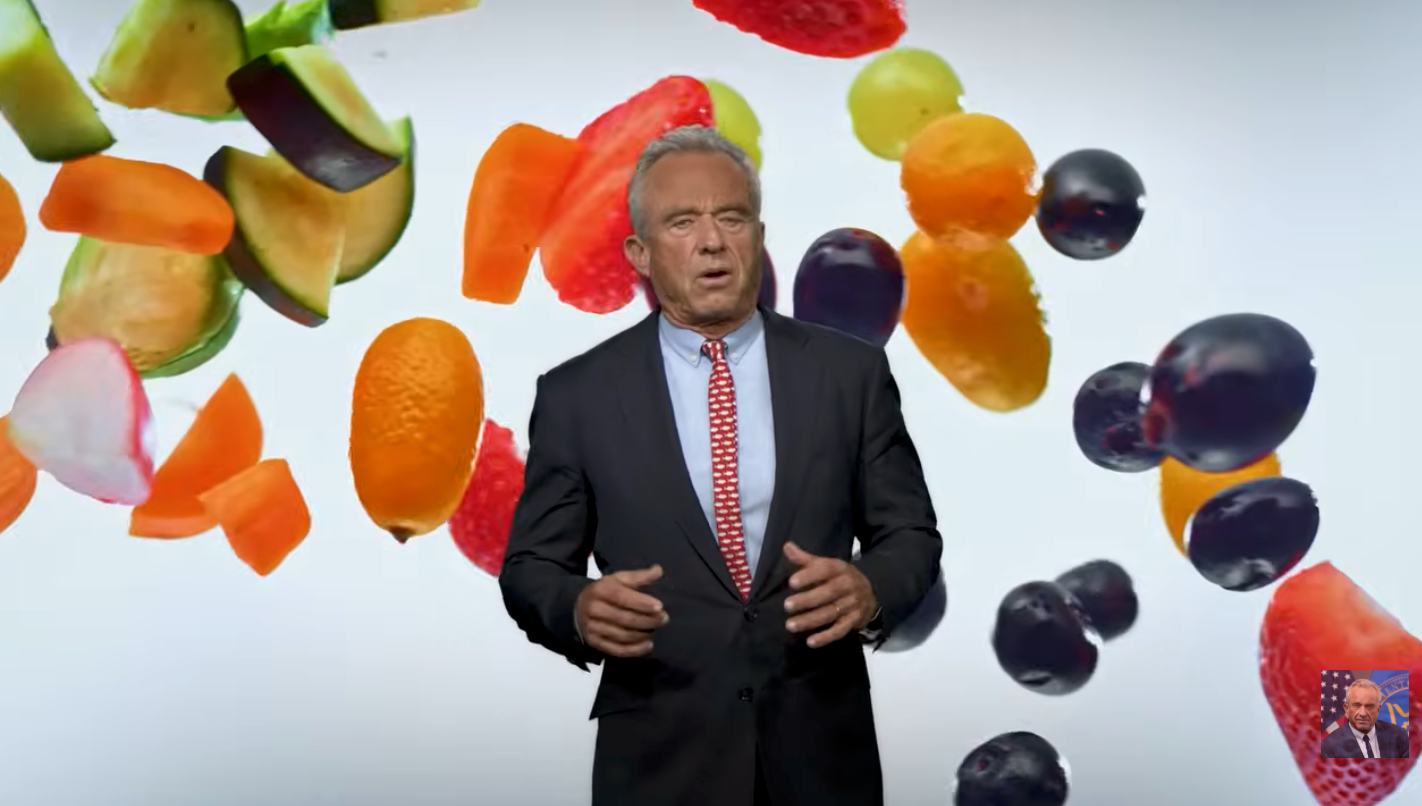 En mann i dress og prikkete slips står mot et bakteppe av flytende frukt og grønnsaker