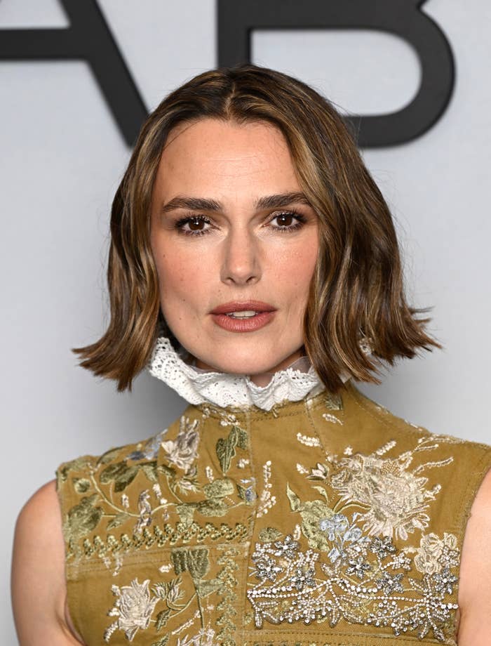 Person with short wavy hair wearing an embroidered, high-collared dress at an event