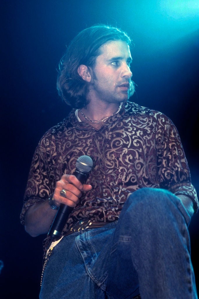 a microphone, wearing patterned shirt and jeans, looking to the side