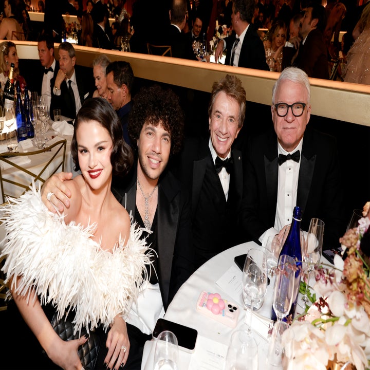 Four people dressed formally at a gala event, smiling at a table. Woman wears a feathered dress, and men wear suits