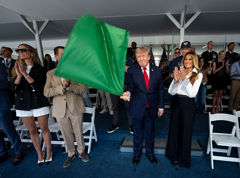 En mann i dress vifter med et grønt flagg på et arrangement. En kvinne står ved siden av ham og klapper. Folk i bakgrunnen ser på og applauderer