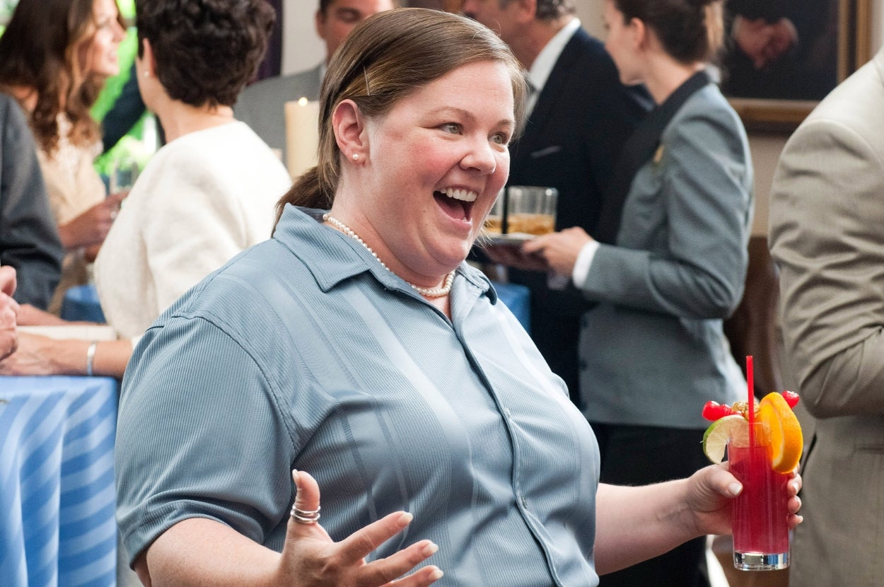 Person in a casual outfit at a social event, smiling and holding a cocktail with a slice of lime and orange garnish