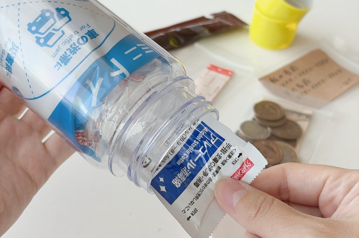 ペットボトルに乾燥剤を入れる手元。バックグラウンドにコインや袋が見える。