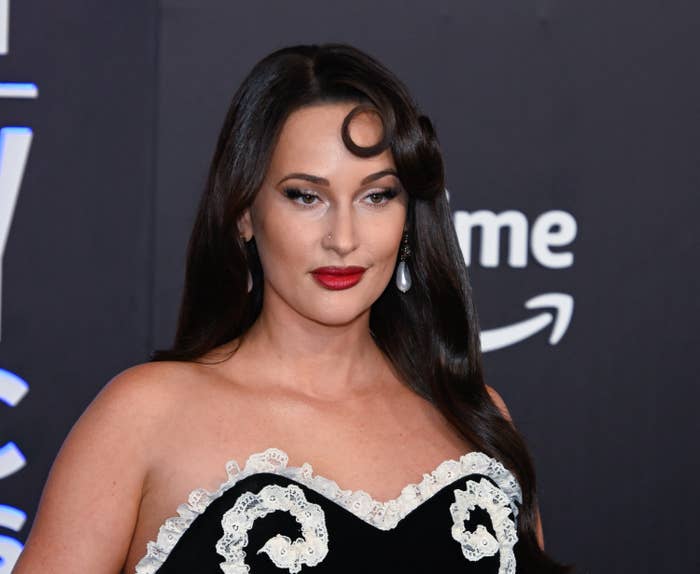 Person on a red carpet wearing an elegant strapless dress with intricate lace details and styled hair with a distinctive curl