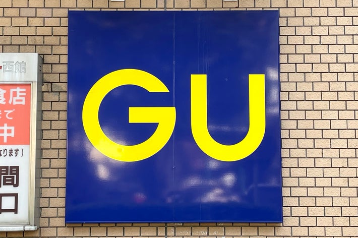 レンガ壁に「GU」と書かれた大きな看板と、隣に飲食店の営業時間が表示された案内板。