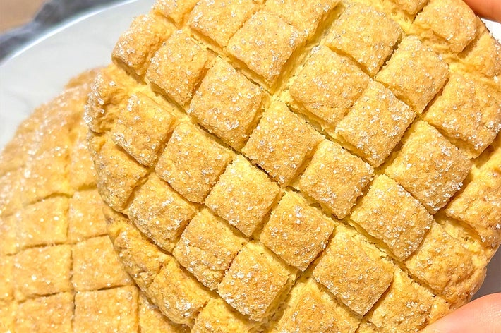 ビスケットのような焼き菓子が2枚、手で持たれている。表面には格子模様と砂糖がかかっている。