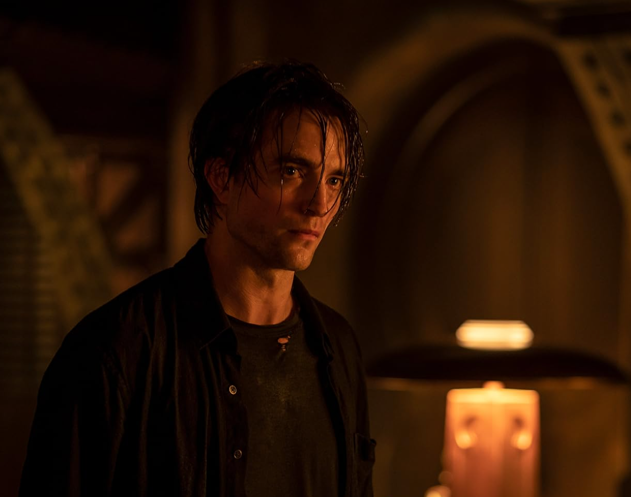 Person in dimly lit room with wet hair, wearing a dark shirt, looking contemplative