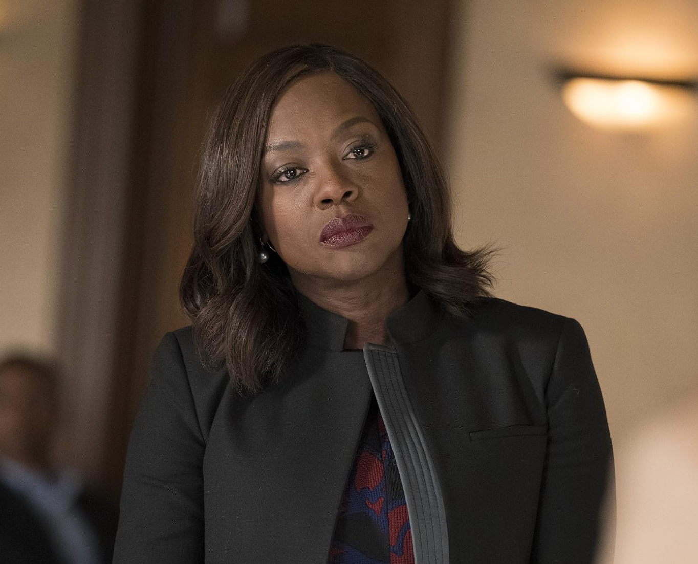 A person in a courtroom setting, wearing a tailored black jacket, appearing thoughtful or concerned