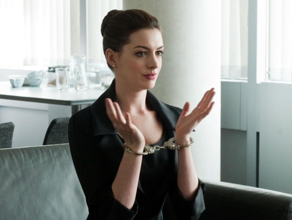 A person sitting on a couch clapping, with hands cuffed together, dressed in formal attire, in a bright room