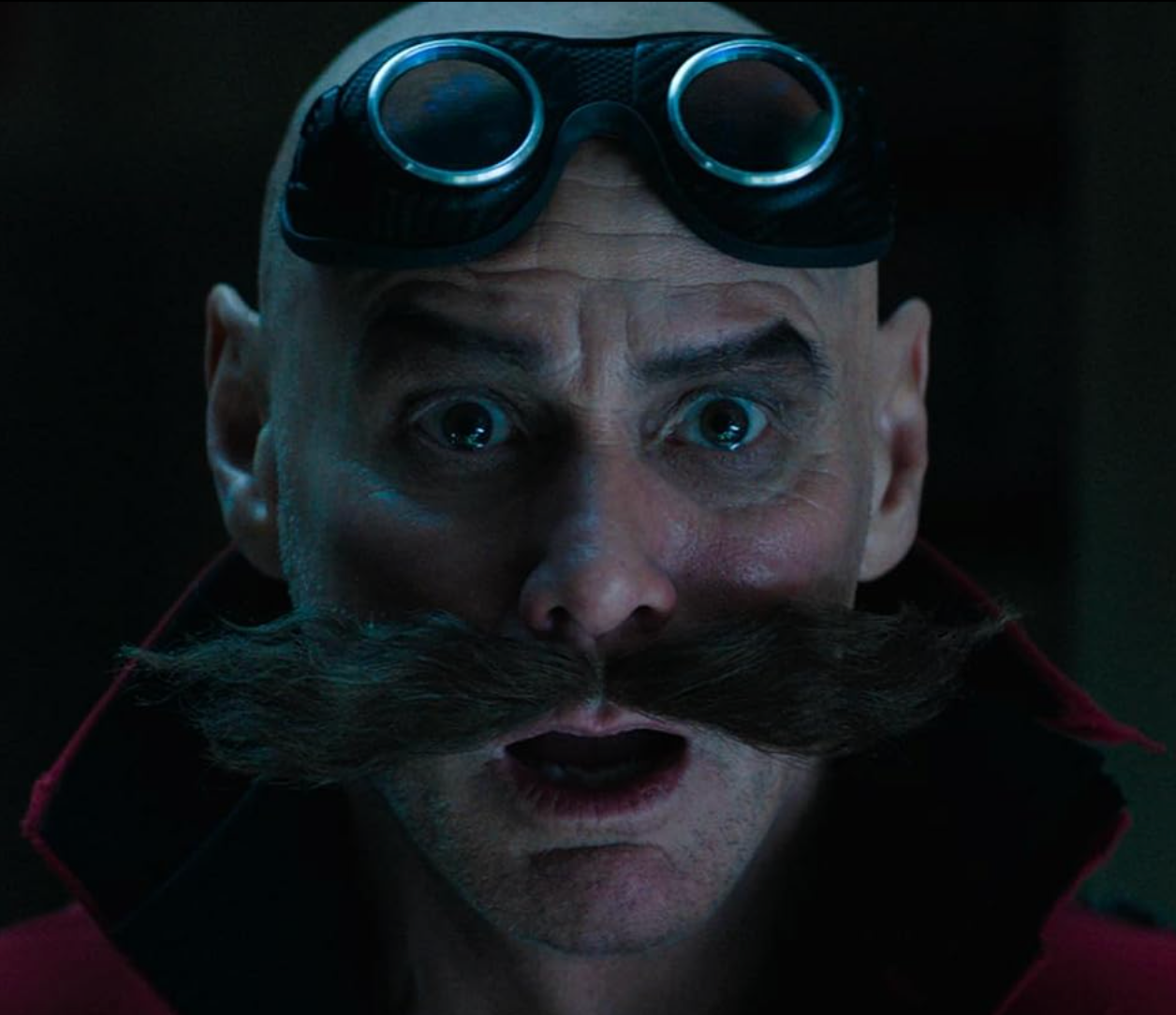 Person with bushy mustache, large round goggles on head, and surprised expression