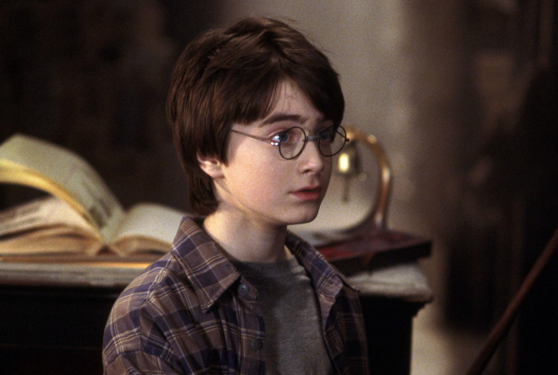 A character with round glasses and a plaid shirt stands indoors, with an open book in the background