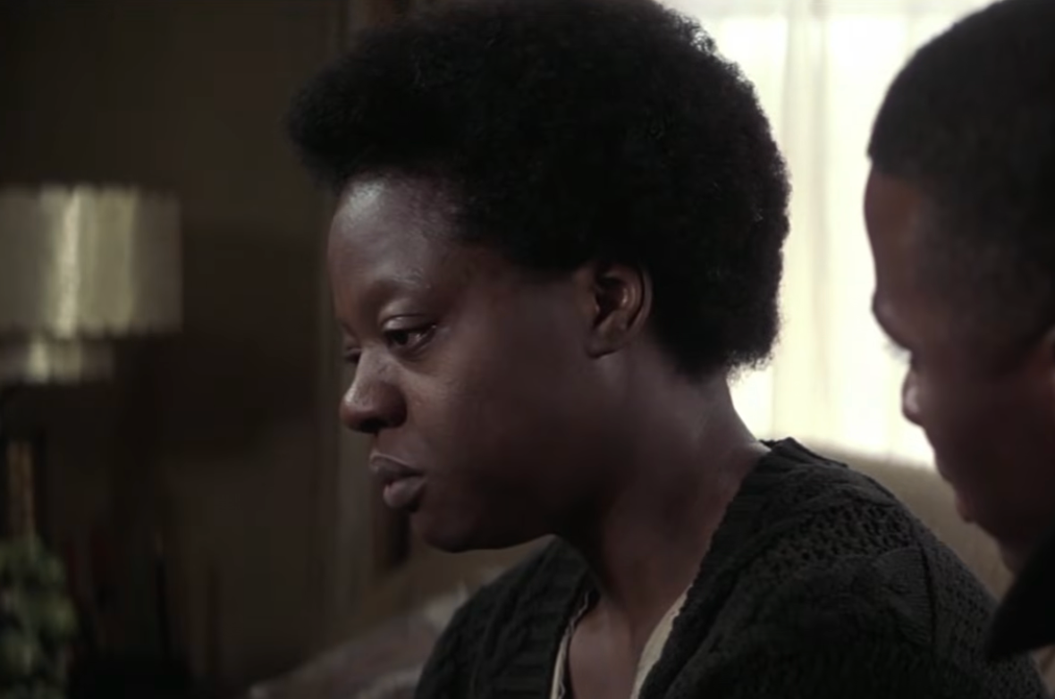Two individuals sit together indoors, both appear thoughtful and engaged in conversation