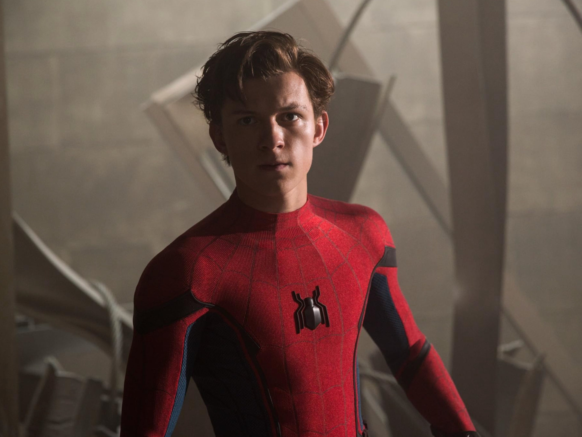 Person in a Spider-Man costume stands indoors with a focused expression, amidst abstract shapes