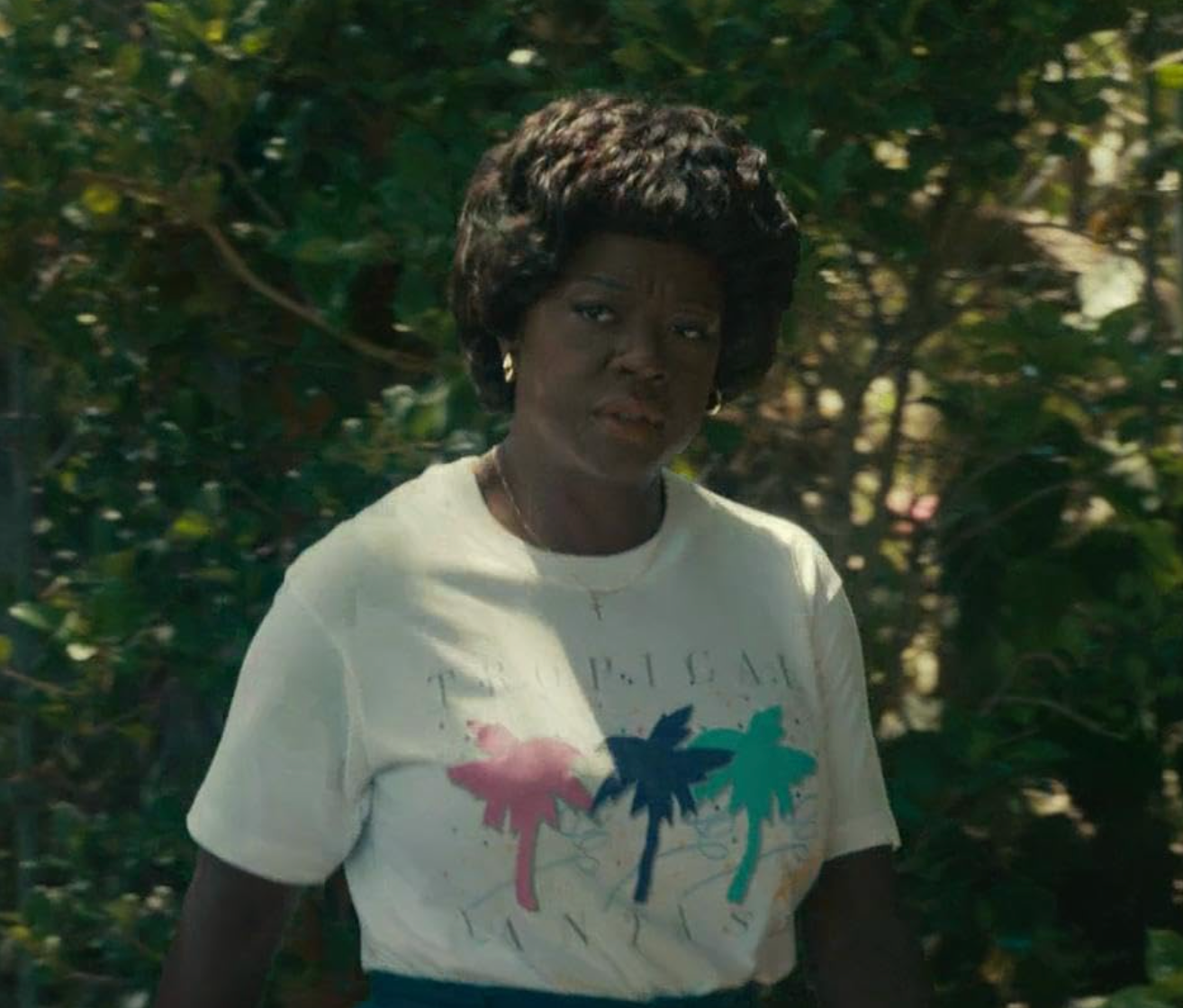 A person outdoors wearing a casual graphic t-shirt with palm trees, standing amid greenery