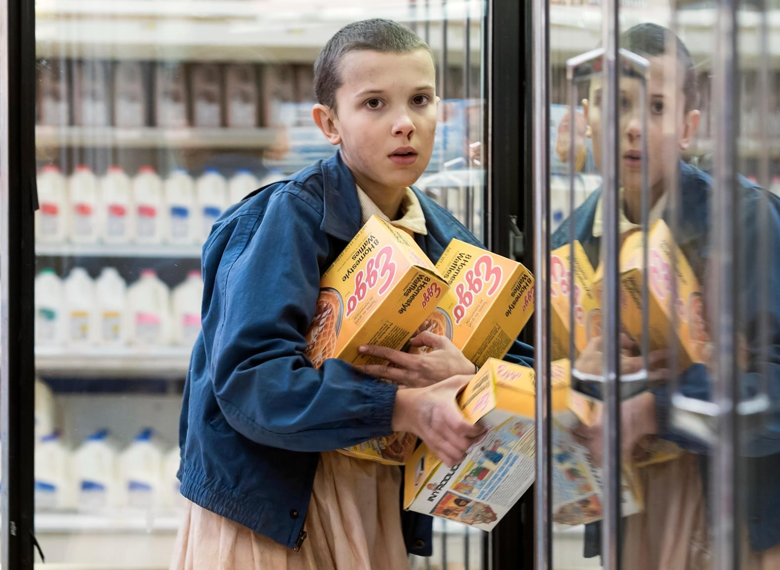 A person with a shaved head holds boxes in a supermarket aisle, looking intently to the side, suggesting they are startled or in a hurry