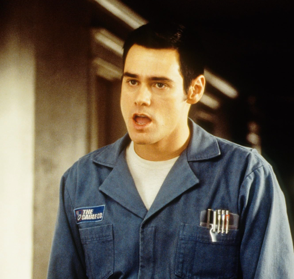 Person in a work uniform with pens in the pocket, standing indoors, appearing to speak or react