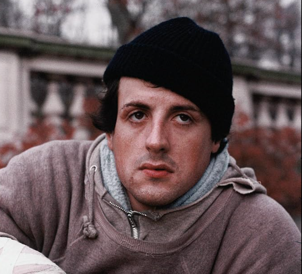 A person in a cozy hoodie and knitted hat gazes thoughtfully outdoors