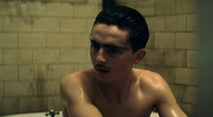 Person with wet hair and a mustache sits in a tiled bathroom, looking contemplative
