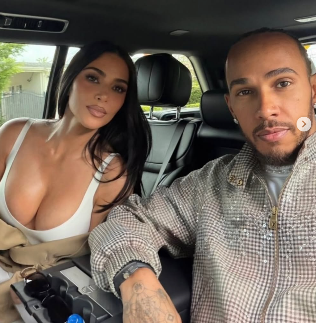 Two people sitting in a car, one wearing a low-cut top and the other in a checkered jacket